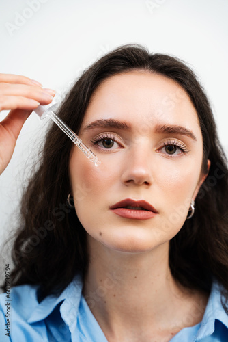 Young woman is applying moisturizing serum on skin face. Girl with hyaluronic acid or serum pipette in hands close-up.