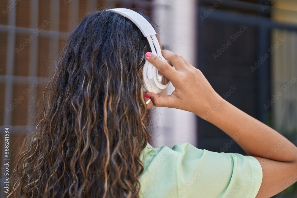 Naklejka premium Young beautiful hispanic woman listening to music at street
