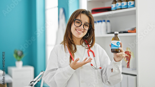 Young beautiful hispanic woman doctor smiling confident presenting medication bottle at clinic