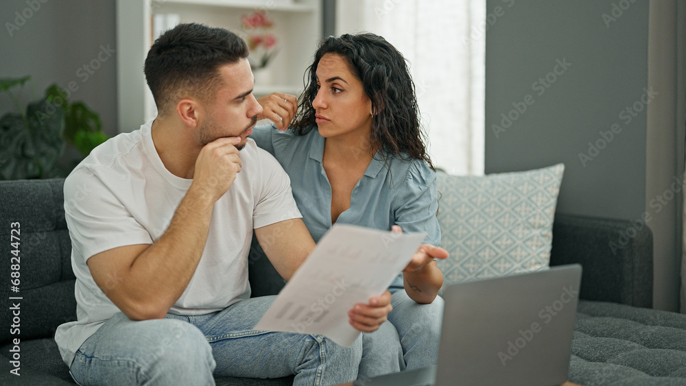 Man and woman couple using laptop reading document looking upset at home Man and woman couple using laptop reading document looking upset at home