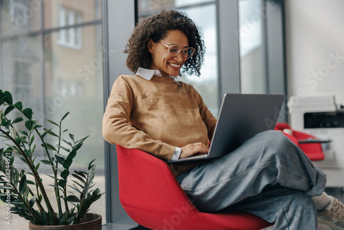 Pretty female freelancer working on laptop while sitting on modern coworking background
