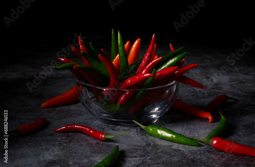 Assorted colorful varieties hot chili peppers in a glass bowl against a dark background.