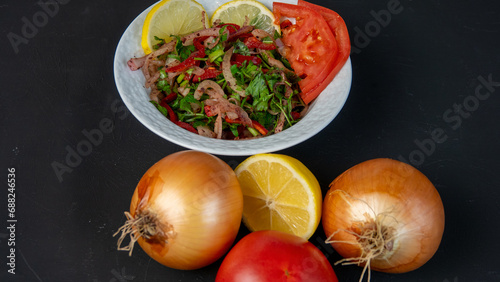 Salad with sliced lemon, onion, parsley and tomatoes in porcelain bowl on dark background. Black background is decorated with onion, tomatoes, lemon. Vegetarian low calorie dish. Healthy diet.