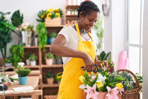 Middle age african american woman florist cutting plants at flower shop photo
