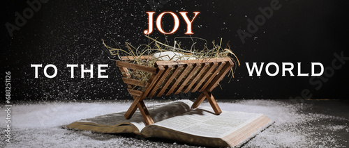 Manger with dummy of baby, Holy Bible and snow on dark background. Concept of Christmas story