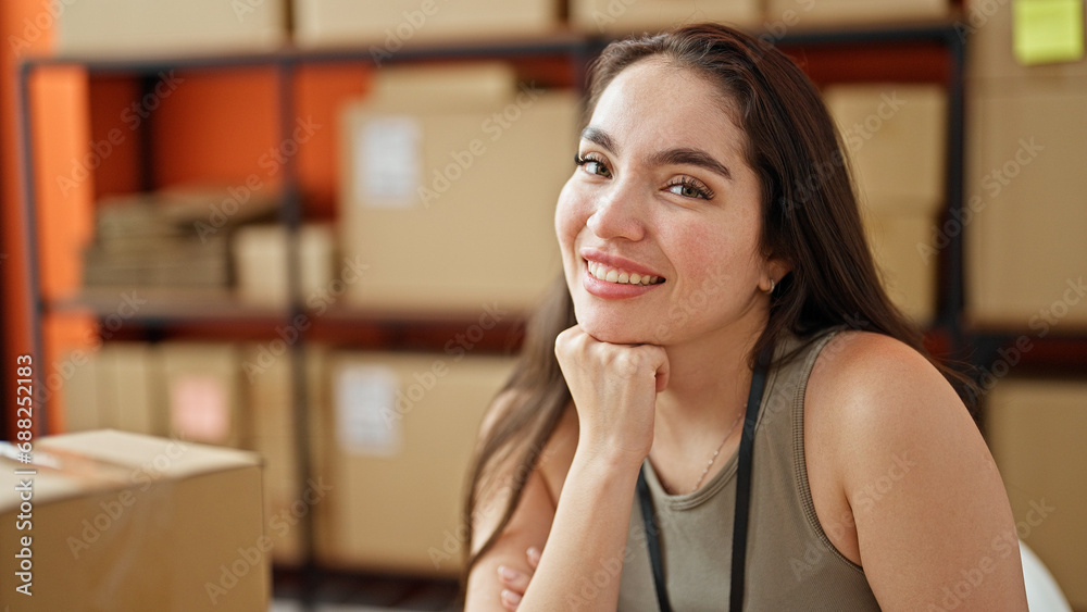 Young beautiful hispanic woman ecommerce business worker smiling confident sitting on table at office Young beautiful hispanic woman ecommerce business worker smiling confident sitting on table at office