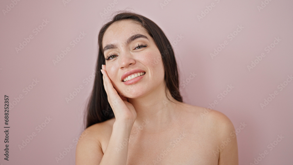 Obraz premium Young beautiful hispanic woman smiling confident touching face over isolated pink background