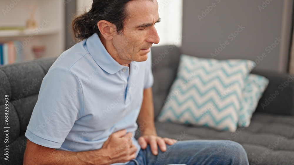 Middle age man suffering for stomach ache sitting on sofa at home