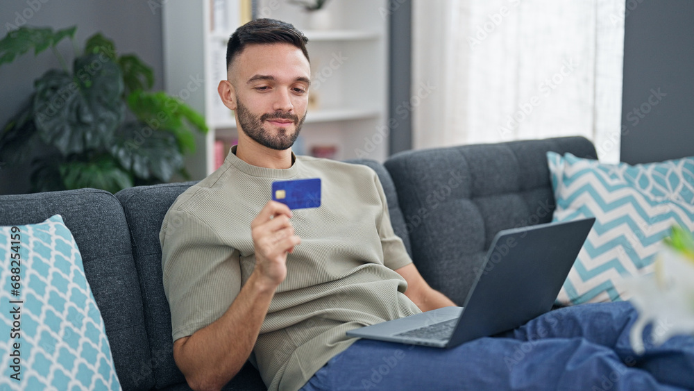 Young hispanic man shopping with laptop and credit card sitting on sofa at home Young hispanic man shopping with laptop and credit card sitting on sofa at home