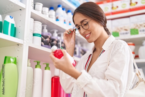 Young beautiful hispanic woman customer reading medication label bottle at pharmacy