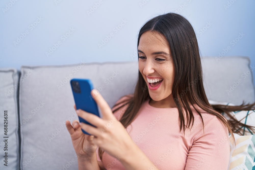 Young beautiful hispanic woman using smartphone sitting on sofa at home