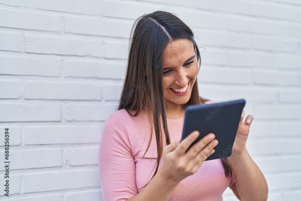 Fototapeta premium Young beautiful hispanic woman smiling confident using touchpad over isolated white brick background
