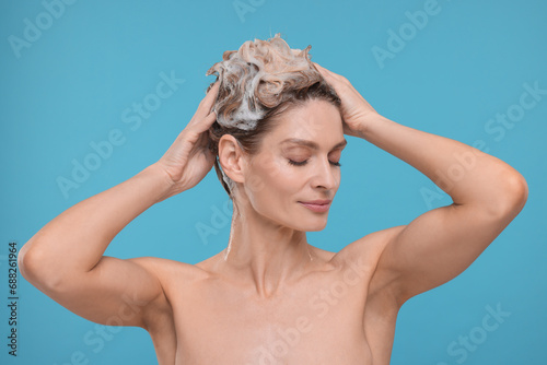 Beautiful woman washing hair on light blue background