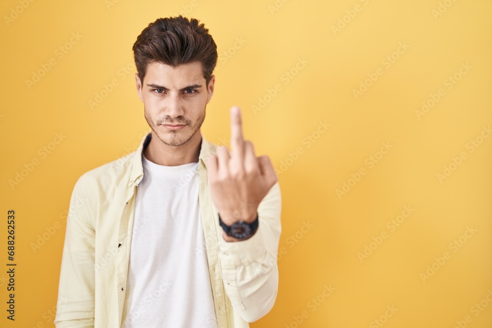 Young hispanic man standing over yellow background showing middle finger, impolite and rude fuck off expression Young hispanic man standing over yellow background showing middle finger, impolite and rude fuck off expression