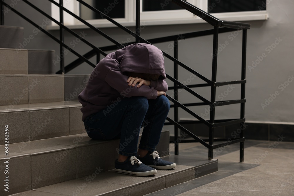 Fototapeta premium Child abuse. Upset boy sitting on stairs indoors