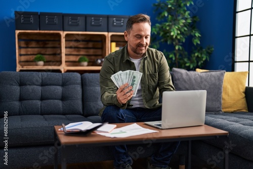 Wallpaper Mural Young caucasian man using laptop counting dollars at home Torontodigital.ca