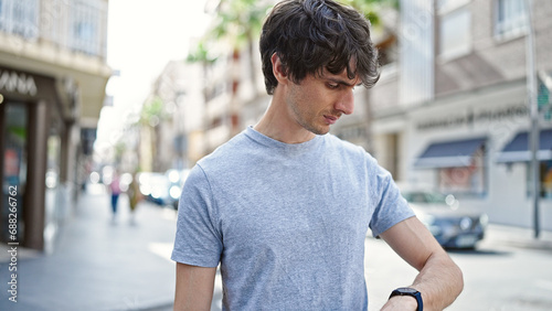 Young hispanic man looking at the watch with serious face at street