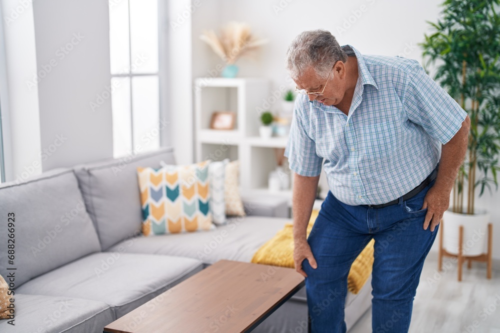 Middle age grey-haired man suffering for knee injury standing at home Middle age grey-haired man suffering for knee injury standing at home