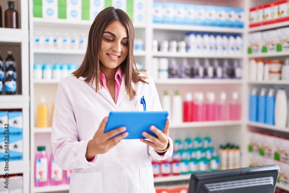 Young beautiful hispanic woman pharmacist using touchpad working at pharmacy