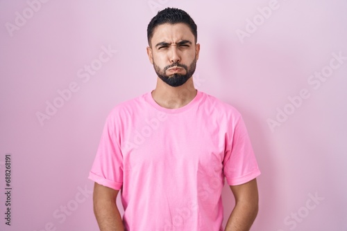 Hispanic young man standing over pink background puffing cheeks with funny face. mouth inflated with air, crazy expression. photo