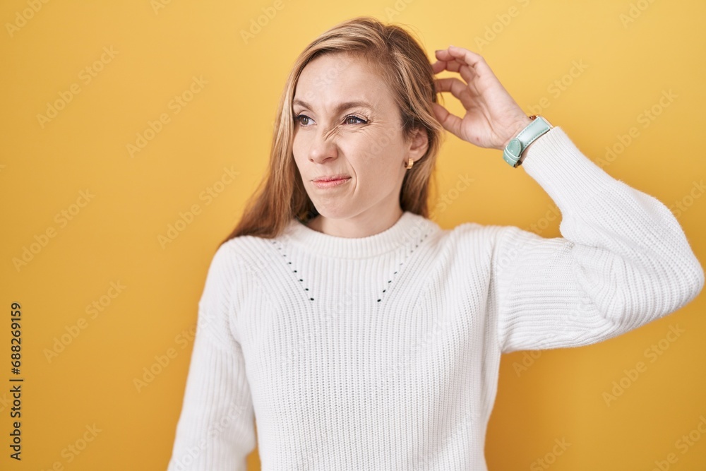Young caucasian woman wearing white sweater over yellow background confuse and wondering about question. uncertain with doubt, thinking with hand on head. pensive concept. Young caucasian woman wearing white sweater over yellow background confuse and wondering about question. uncertain with doubt, thinking with hand on head. pensive concept.