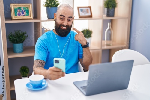 Young hispanic man with beard and tattoos doing video call with smartphone smiling happy pointing with hand and finger
