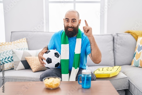 Young hispanic man with beard and tattoos football hooligan holding ball supporting team surprised with an idea or question pointing finger with happy face, number one © Krakenimages.com