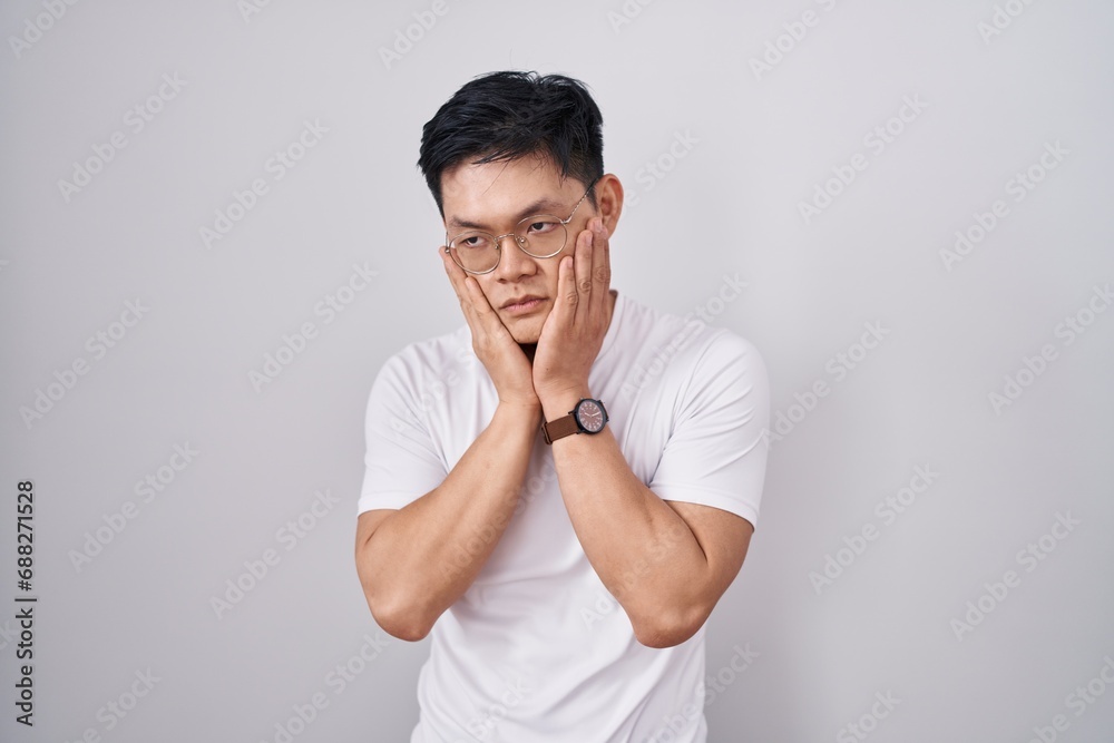 Young asian man standing over white background tired hands covering face, depression and sadness, upset and irritated for problem