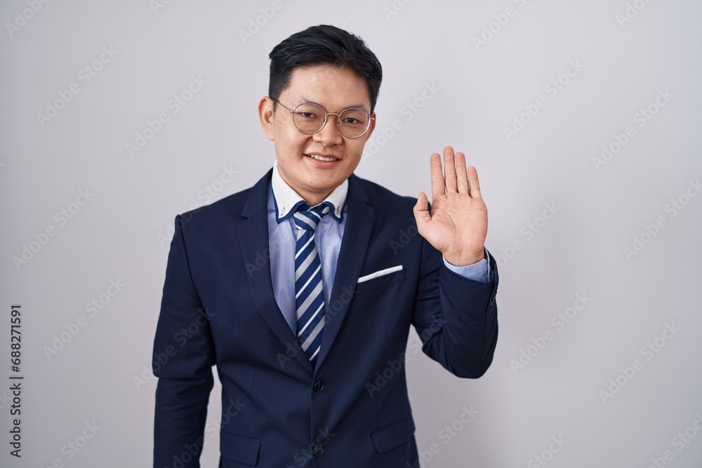 Young asian man wearing business suit and tie waiving saying hello happy and smiling, friendly welcome gesture Young asian man wearing business suit and tie waiving saying hello happy and smiling, friendly welcome gesture