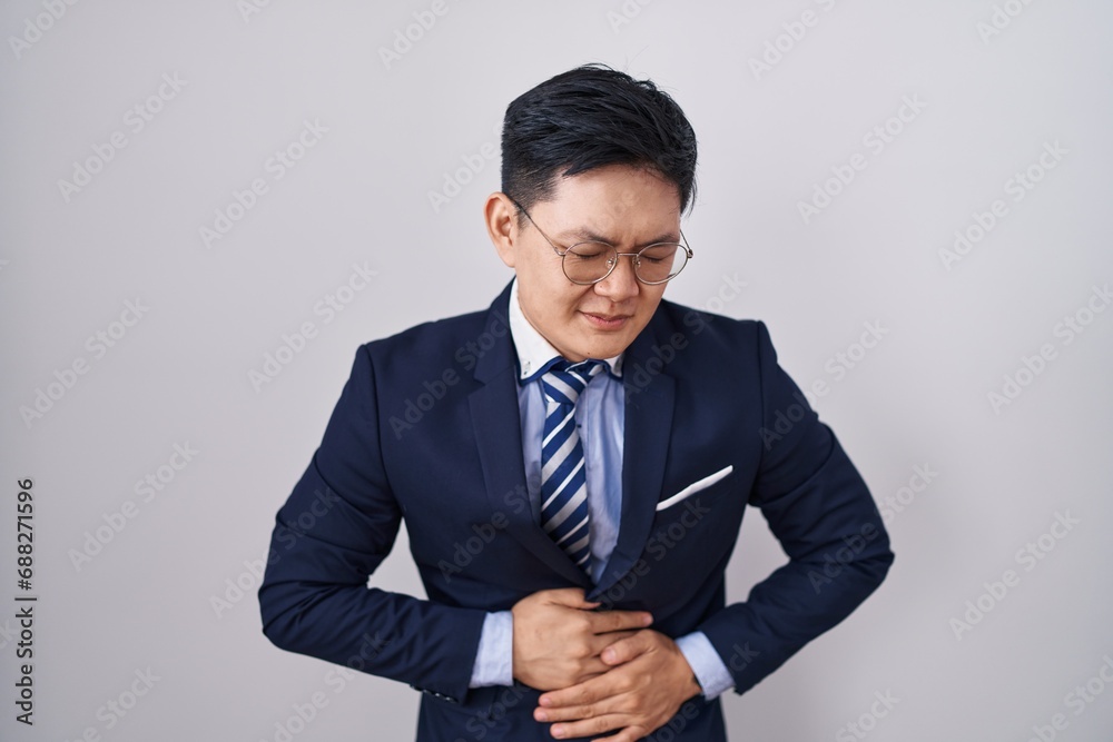 Young asian man wearing business suit and tie with hand on stomach because indigestion, painful illness feeling unwell. ache concept. Young asian man wearing business suit and tie with hand on stomach because indigestion, painful illness feeling unwell. ache concept.