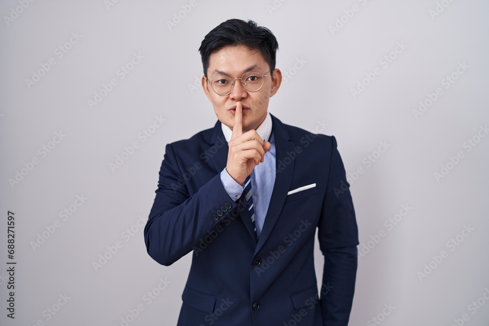 Young asian man wearing business suit and tie asking to be quiet with finger on lips. silence and secret concept. Young asian man wearing business suit and tie asking to be quiet with finger on lips. silence and secret concept.
