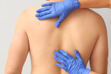 Dermatologist examining moles on young man's back against light background, closeup