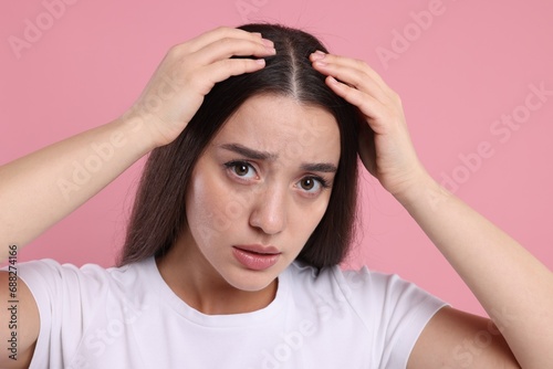 Sad woman examining her hair and scalp on pink background. Dandruff problem
