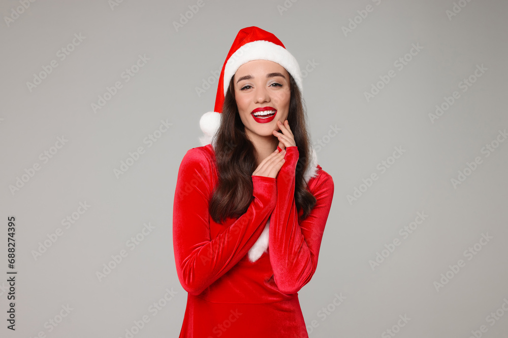 Christmas celebration. Beautiful young woman in red dress and Santa hat on grey background Christmas celebration. Beautiful young woman in red dress and Santa hat on grey background