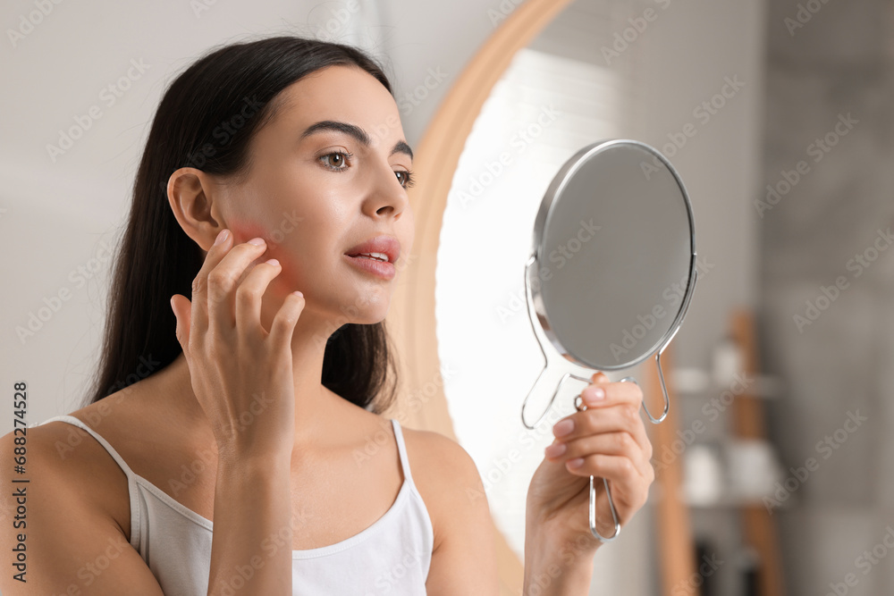 Suffering from allergy. Young woman looking in mirror and scratching her face indoors Suffering from allergy. Young woman looking in mirror and scratching her face indoors