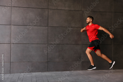 Happy man running near building outdoors. Space for text