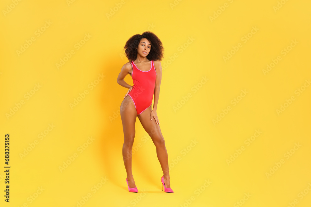 Beautiful woman in bright one-piece summer swimsuit and stylish high heel shoes on yellow background - obrazy, fototapety, plakaty 