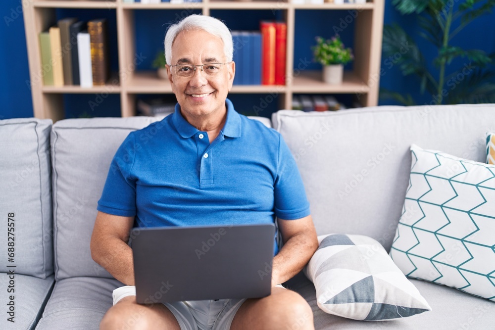 Middle age grey-haired man using laptop sitting on sofa at home Middle age grey-haired man using laptop sitting on sofa at home