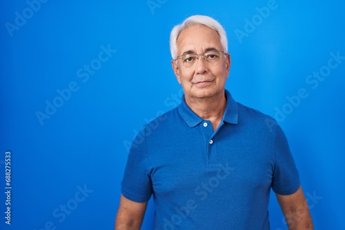 Middle age man with grey hair standing over blue background relaxed with serious expression on face. simple and natural looking at the camera. © Krakenimages.com
