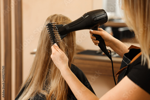 Professional hairdresser drying girl's hair in beauty salon, closeup