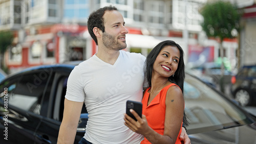 Beautiful couple using smartphone standing by car at street