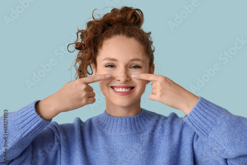 Portrait of pretty young girl pointing at her nose on blue background