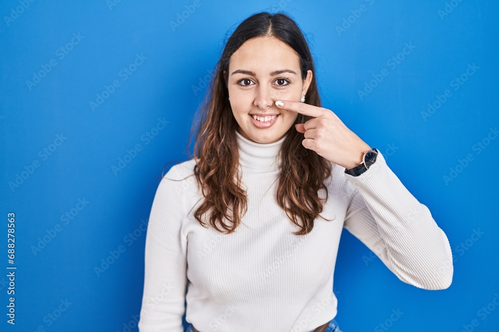 Young hispanic woman standing over blue background pointing with hand finger to face and nose, smiling cheerful. beauty concept Young hispanic woman standing over blue background pointing with hand finger to face and nose, smiling cheerful. beauty concept