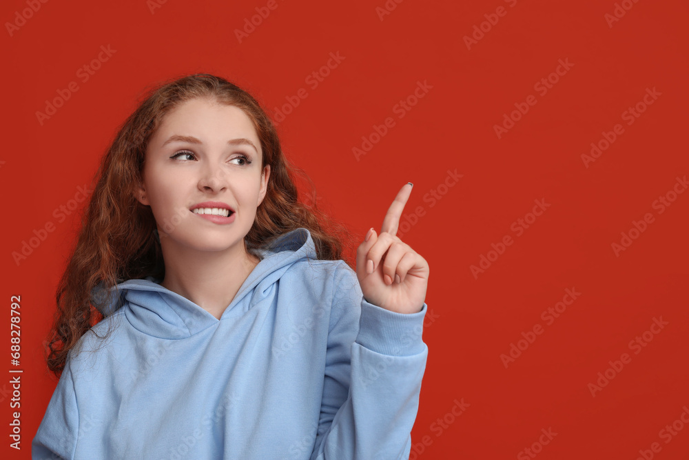 Portrait of ashamed young woman pointing at something on red background Portrait of ashamed young woman pointing at something on red background