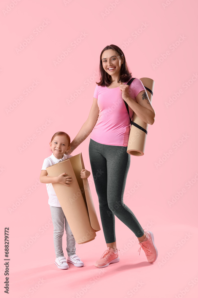 Beautiful mother and her cute little daughter with yoga mats on pink background Beautiful mother and her cute little daughter with yoga mats on pink background