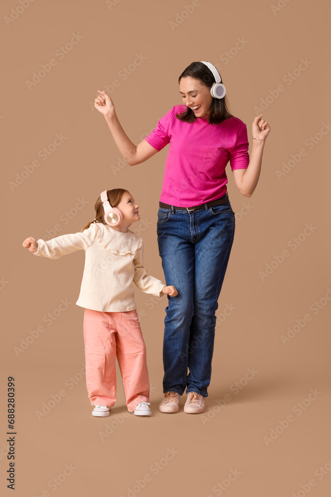 Beautiful mother with her cute little daughter in headphones listening music on brown background Beautiful mother with her cute little daughter in headphones listening music on brown background