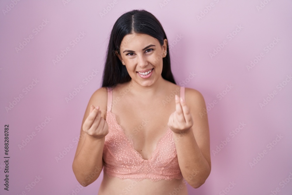 Young hispanic woman wearing pink bra doing money gesture with hands, asking for salary payment, millionaire business Young hispanic woman wearing pink bra doing money gesture with hands, asking for salary payment, millionaire business