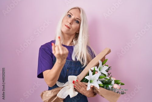 Caucasian woman holding bouquet of white flowers showing middle finger, impolite and rude fuck off expression