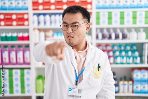 Chinese young man working at pharmacy drugstore pointing displeased and frustrated to the camera, angry and furious with you © Krakenimages.com
