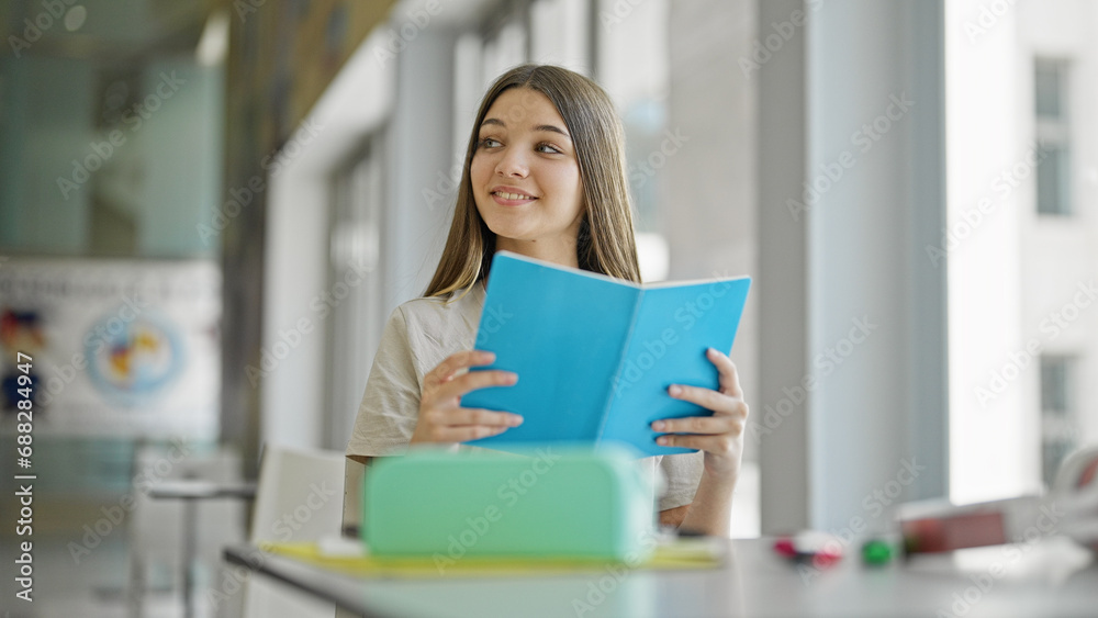 Young beautiful girl student reading book smiling at library Young beautiful girl student reading book smiling at library